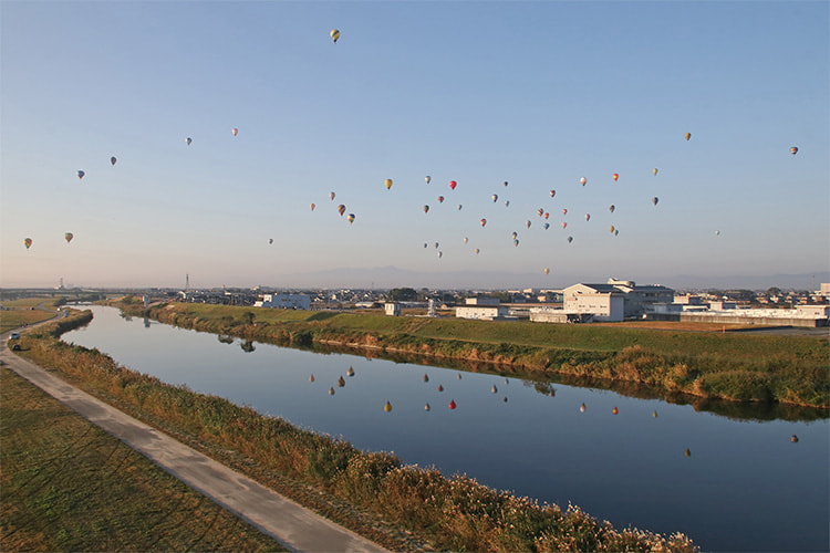 たくさんの熱気球が飛び、川にその姿が写っている写真