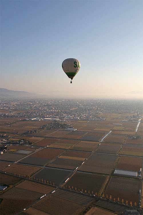 下方に広がる田園地帯上を１機、逆光を浴びシルエットとなった熱気球の写真